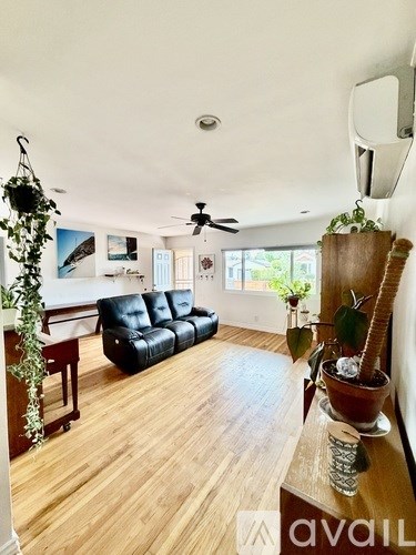 A living room with a black leather sofa and wooden flooring.