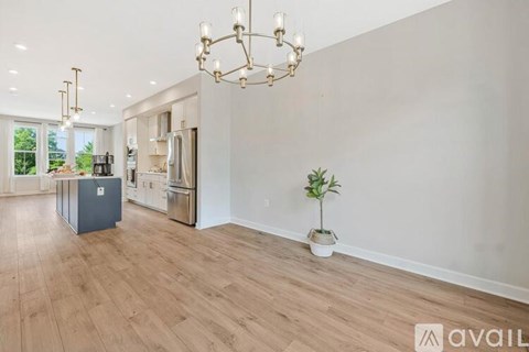 A spacious room with a chandelier, a potted plant, and a kitchen area in the background.