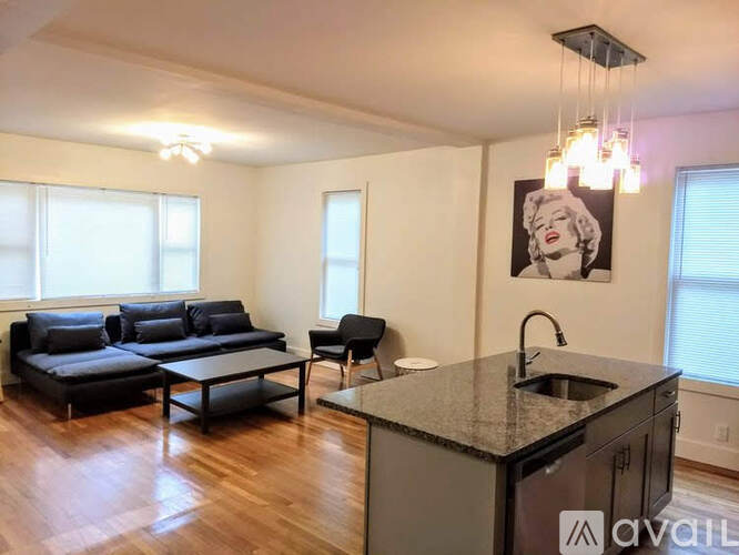 A kitchen area with a sink and a countertop with a chair and a couch in the background.