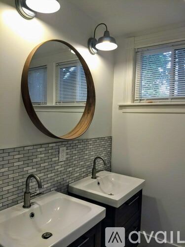 A bathroom with two sinks and a round mirror.