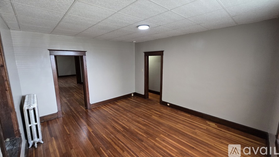 A room with wooden flooring and white walls, with a door and a mirror on the wall.