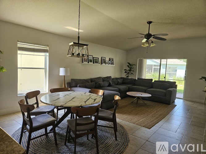 A living room with a grey sofa, a round table with chairs, and a ceiling fan.