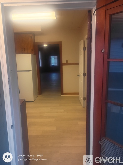 A hallway with a refrigerator on the left and a red door on the right.