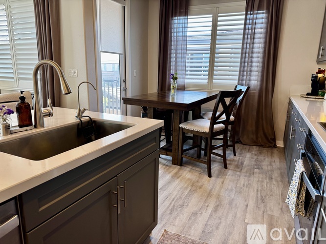 A kitchen with a sink, a table and chairs, and a window with curtains.