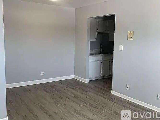 A room with a grey floor and a white wall with a fridge in it.