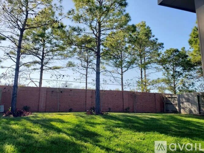 A grassy area with trees and a red brick wall in the background.