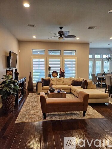 A living room with a brown sofa and a ceiling fan.