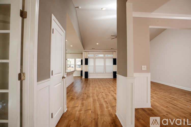 A room with wooden floors and white walls, with a door on the left and a window on the right.