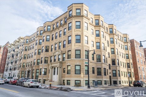 A large, beige building with many windows is situated on a street corner.