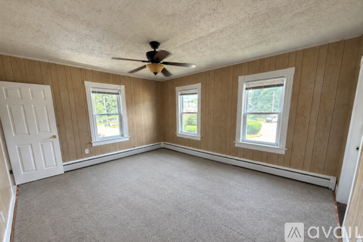 A room with a carpeted floor, a ceiling fan, and three windows.