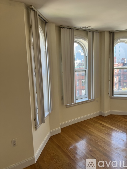 A room with wooden floors and three windows with curtains.