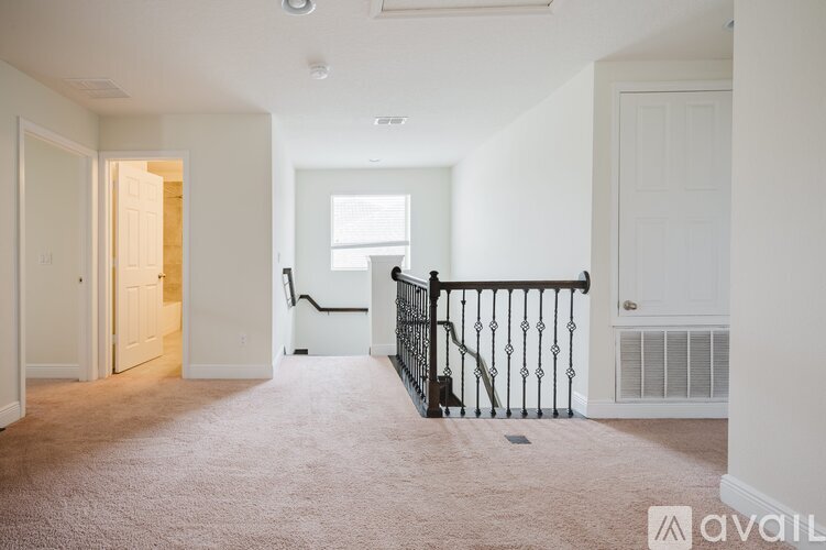 A spacious living room with a carpeted floor and a staircase with a black railing.