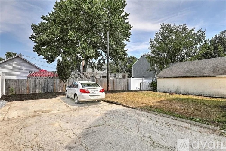 A car is parked in a driveway with a house and a tree in the background.