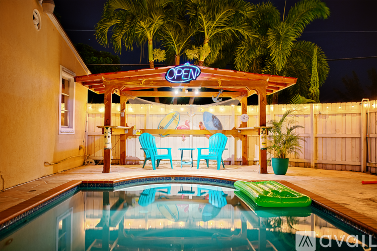 A poolside area with a table and chairs under a lit up sign that says "OPEN".