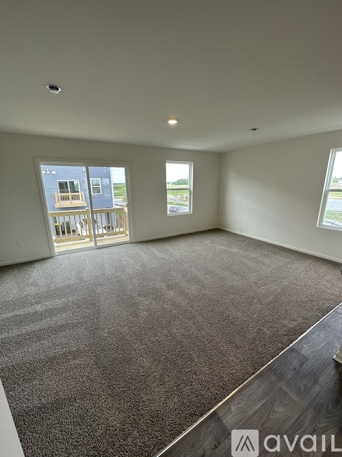 A room with grey carpet and two windows overlooking a balcony.