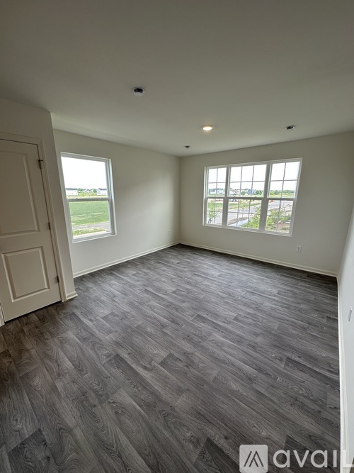 A room with wooden flooring and two windows overlooking a field.