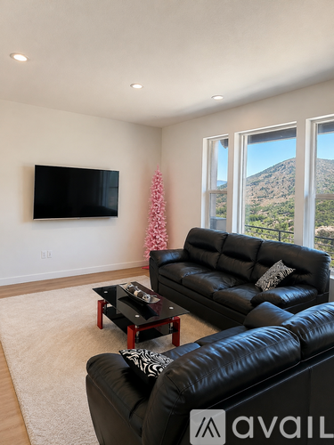 A living room with a black leather couch and a flat screen TV mounted on the wall.