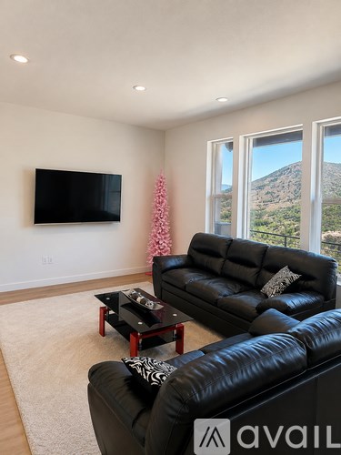 A living room with a black leather couch and a flat screen TV mounted on the wall.