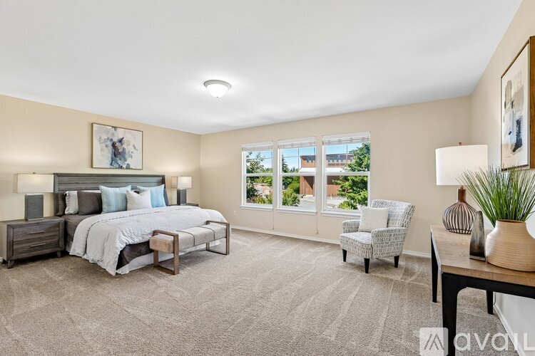 A bedroom with a large bed, a chair, and a table with a vase on it.