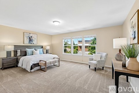 A bedroom with a large bed, a chair, and a table with a vase on it.