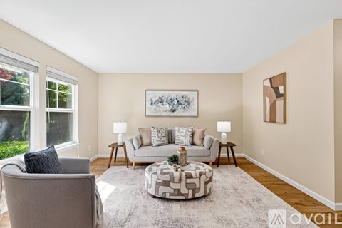 A living room with a grey couch, a patterned ottoman, and a painting on the wall.