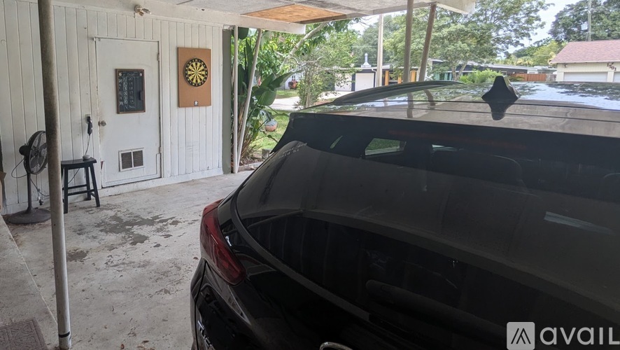 A black car is parked in front of a white building with a brown door.