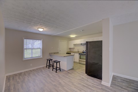 A kitchen with a black refrigerator and wooden flooring.