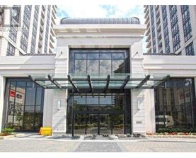 A modern building entrance with a glass canopy and a stone pillar.