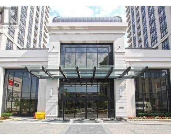 A modern building entrance with a glass canopy and a stone pillar.