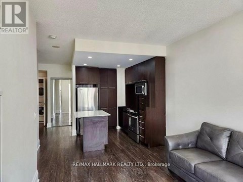 A modern kitchen with dark wood cabinets and a grey sofa in the foreground.