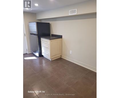 A kitchen area with a black fridge and a black flat screen TV on a cabinet.