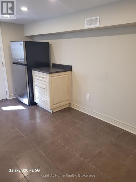 A kitchen area with a black fridge and a black flat screen TV on a cabinet.