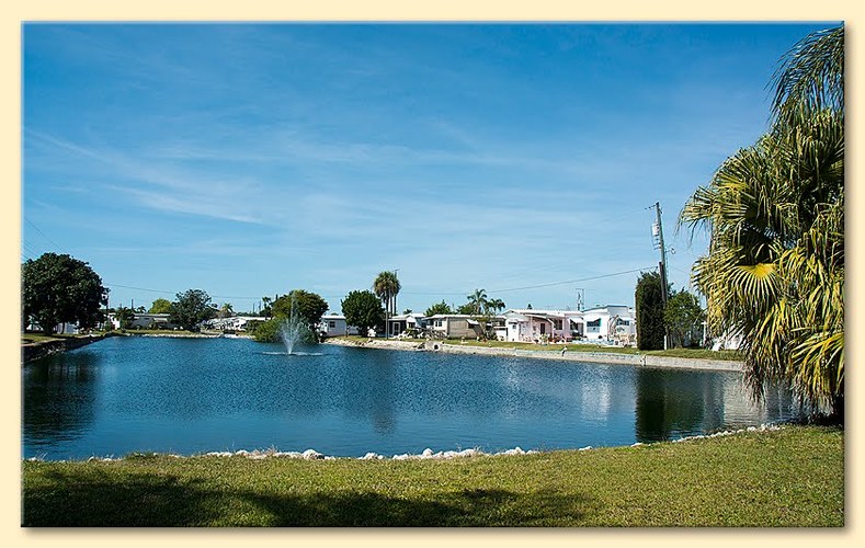 A serene lake with a fountain in the middle surrounded by houses and trees.