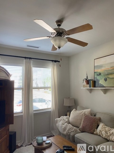A living room with a couch, a coffee table, a ceiling fan, and a painting on the wall.