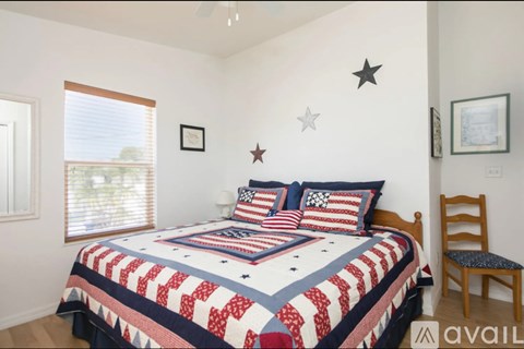 A bedroom with a bed covered in a quilt with red, white and blue patterns and a wooden chair.