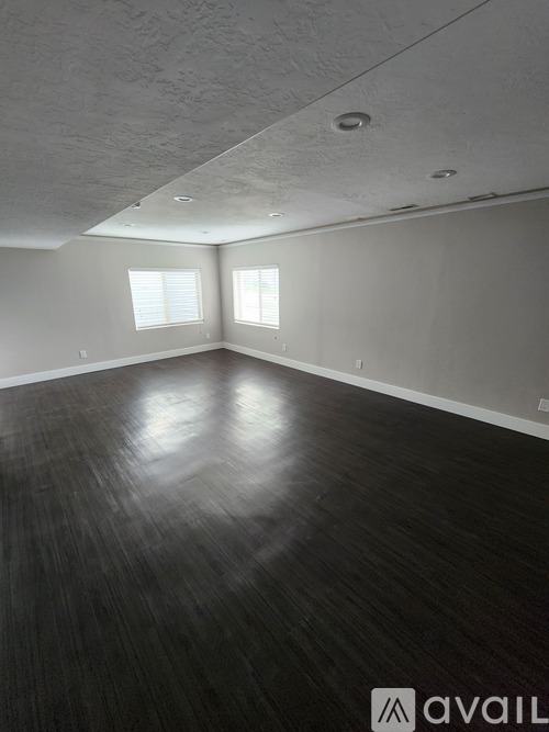 A room with wooden flooring and two windows.
