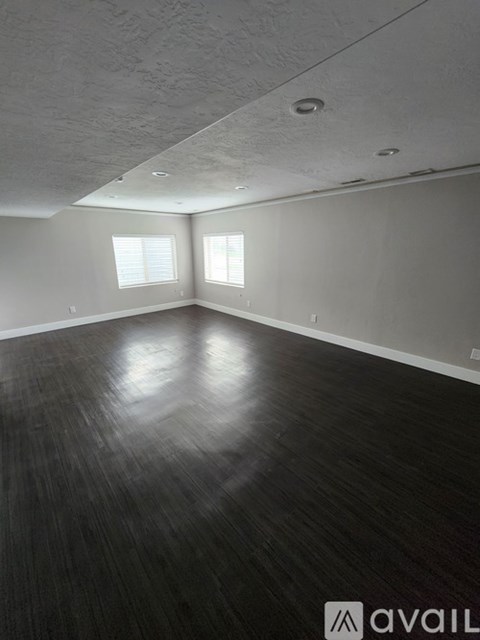 A room with wooden flooring and two windows.