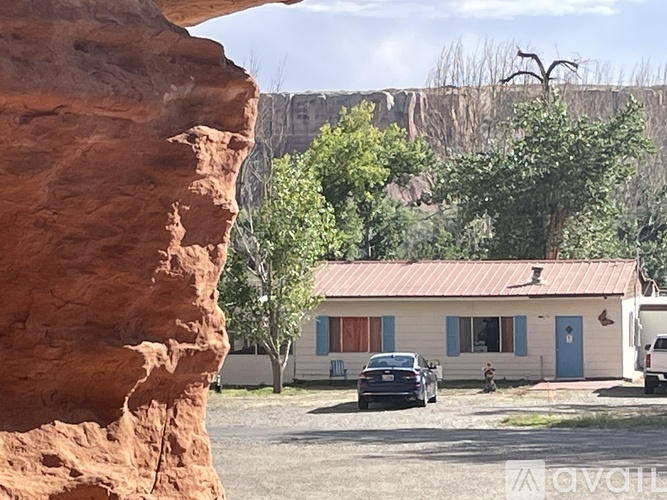 A house with a blue door is situated in front of a large rock formation.
