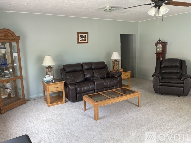 A living room with a black leather couch, a wooden coffee table, and a wooden side table with a lamp.