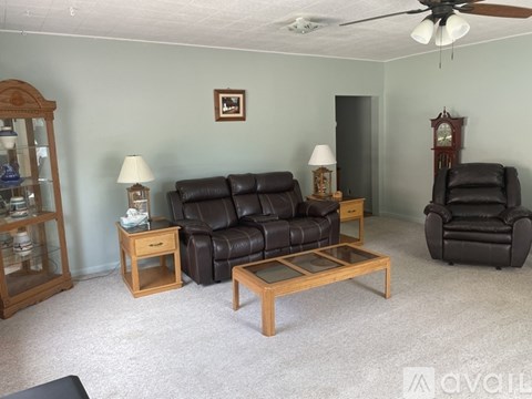 A living room with a black leather couch, a wooden coffee table, and a wooden side table with a lamp.