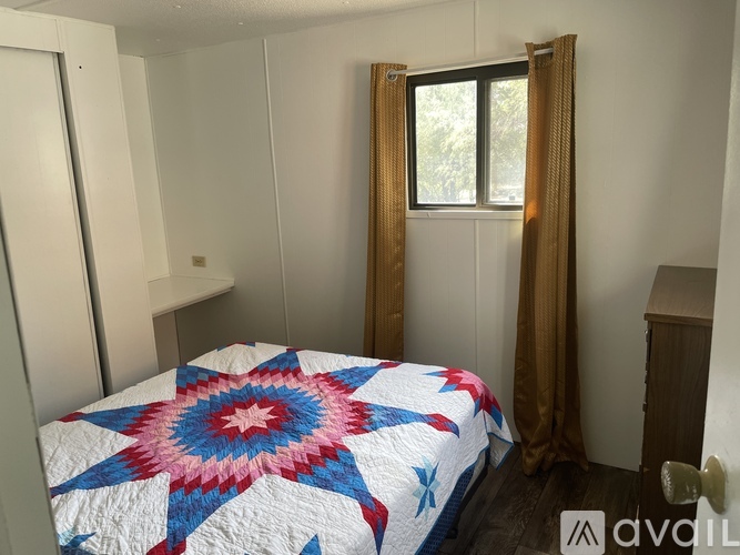 A bedroom with a bed covered in a quilt with a star pattern and a window with curtains.