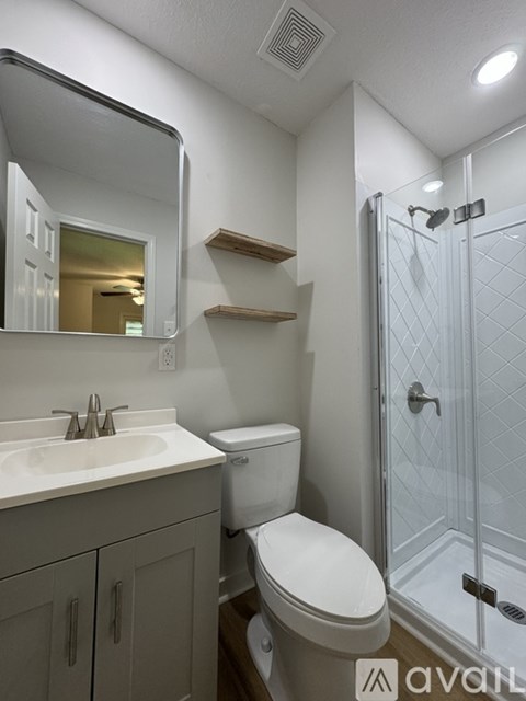 A bathroom with a toilet, sink, mirror, and shower.