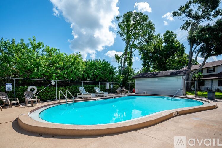 A swimming pool surrounded by trees and a fence with chairs around it.