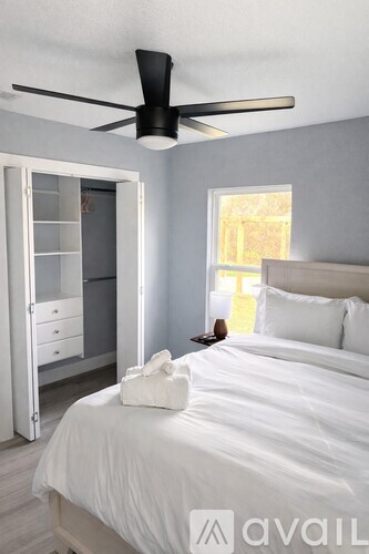 A bedroom with a white bed and a ceiling fan.