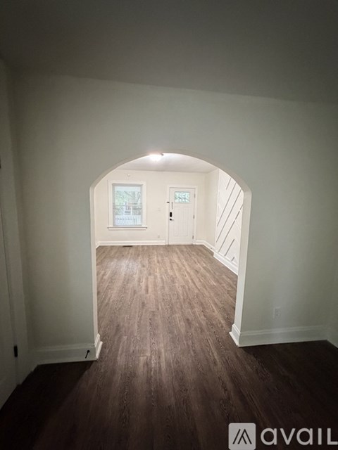 A room with a wooden floor and a white archway leading to another room.
