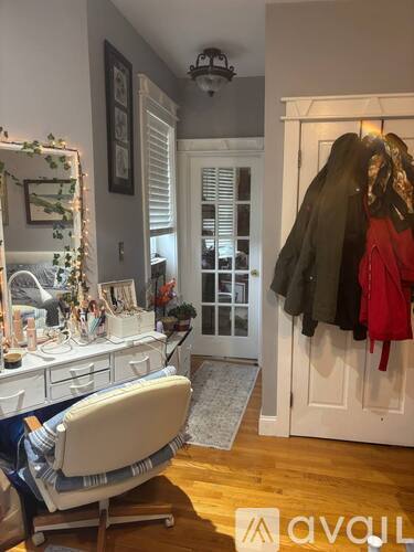 A room with a desk, chair, and a coat rack with clothes hanging on it.