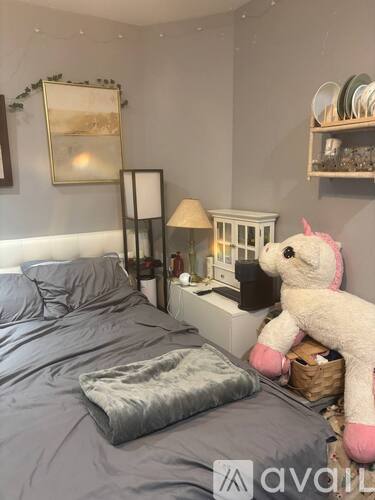 A bedroom with a bed, a nightstand with a lamp, and a shelf with plates.