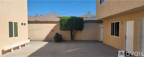 A small tree is in the corner of a tan-colored house with a white door and window.
