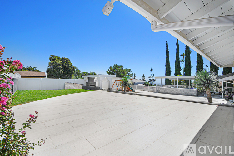 A large, empty patio area with a white pergola and a playground in the background.
