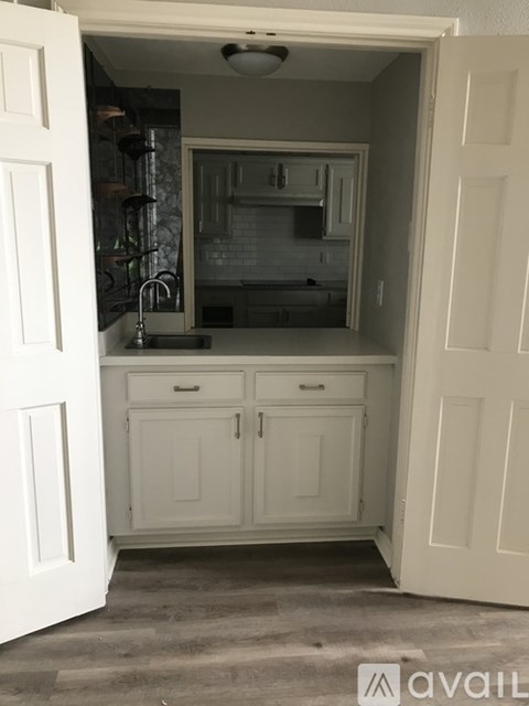 A kitchen with white cabinets and a sink is visible through an open door.